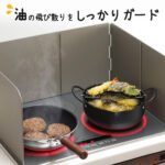 [下村]可伸縮防油板伸展後放在電子爐旁邊，圍着兩個正在煮食的鍋具。