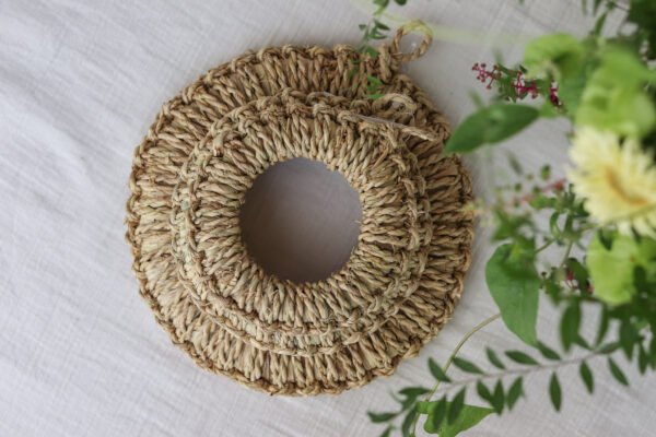兩個大小不同的日本手工製草編 鍋墊/ 鍋敷疊放的俯視圖，旁邊有花束，背景為白色