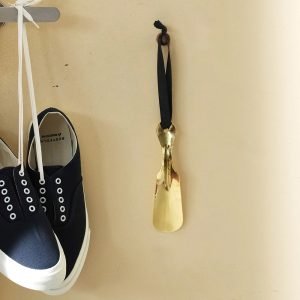 黃銅製鞋拔掛在牆上的照片,展示其光亮的金屬質感和精美設計。 Picture of a brass shoehorn hanging on the wall, showcasing its shiny metal texture and elegant design.