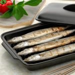 日本製造陶瓷烤盤側邊放置耐熱蓋，內含4條並排烤魚. A Japanese ceramic baking tray with the lid on its side, containing 4 baked fish side by side inside.