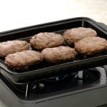 日本製造陶瓷烤盤內含6個漢堡扒，放置在小型氣體爐的上方. A Japanese ceramic baking tray with 6 pieces of burger patties inside, placed on top of a small gas stove.