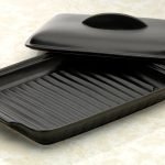 日本製造陶瓷烤盤的耐熱蓋半開，擱放在盤邊，清晰可見內部底部的設計。 Close-up of the Japanese-made ceramic baking tray with the heat-resistant lid half open, resting at the edge, revealing the inside bottom of the tray.