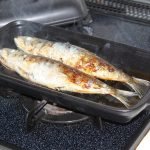 日本製陶瓷烤盤（S號）在爐子上烤魚，耐熱蓋擱置在旁。 Japanese-made ceramic baking tray (size S) baking fish on a stove, with the heat-resistant lid placed beside it.