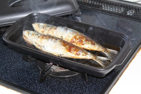 日本製陶瓷烤盤（S號）在爐子上烤魚，耐熱蓋擱置在旁。 Japanese-made ceramic baking tray (size S) baking fish on a stove, with the heat-resistant lid placed beside it.