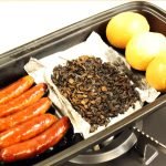 日本製造陶瓷烤盤內含香腸、雞蛋及其他食物，擺放在爐子上。 Japanese-made ceramic baking tray containing sausages, eggs, and other foods, placed on top of a stove.