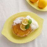 檸檬形狀的黃色淺碗，上面放著煎餅 - Yellow lemon-shaped shallow bowl with a pancake on top.