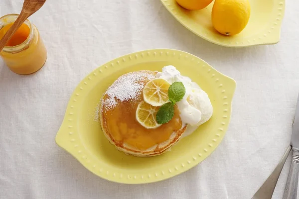 檸檬形狀的黃色淺碗，上面放著煎餅 - Yellow lemon-shaped shallow bowl with a pancake on top.