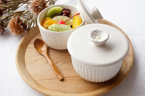 兩個Yoshizawa 益子燒茶碗蒸杯放在圓形托盤上,一個蓋著蓋子,另一個打開顯示裡面的甜點 - Two Yoshizawa Mashiko-style chawanmushi cups on a round tray, one covered with a lid and the other open revealing the dessert inside.