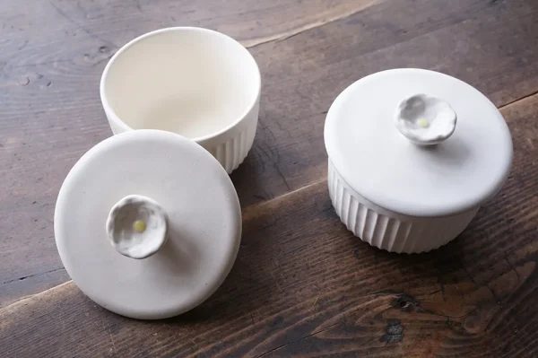 兩個Yoshizawa 益子燒茶碗蒸杯放在桌面上,左側的杯子蓋子放在杯旁,右側的杯子蓋著蓋子 - Two Yoshizawa Mashiko-style chawanmushi cups on a tabletop, with the left cup's lid beside it and the right cup covered.