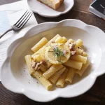 Yoshizawa 益子燒雲邊深盤上放著義大利麵，擺放在桌上，清楚展示雲朵設計的邊緣 - Yoshizawa Mashiko-style cloud-edged deep plate with pasta on it, placed on a table, clearly showing the cloud design edge