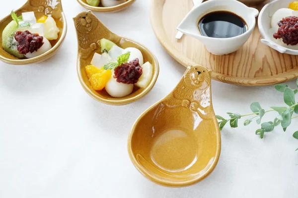 三個Yoshizawa 益子燒碟子在餐桌上，前面的盤子空著，後面的兩個盤子盛有食物 - Three Yoshizawa Mashiko-style plates on a dining table, with the front plate empty and the two back plates containing food.