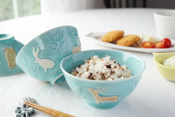 Yoshizawa 益子燒森林動物飯碗內裝米飯，並展示兩個不同側面的碗，擺放在餐桌上。 / Yoshizawa Mashiko-style forest animal rice bowl filled with rice, featuring two bowls shown from different sides on a dining table.