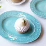 兩個Yoshizawa 益子燒綠色兔子花卉橢圓餐盤放在桌上，每個盤子上都有一個蛋糕 - Two Yoshizawa Mashiko-style green rabbit floral oval plates on a table, each with one cake on them.