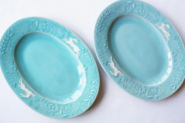 兩個Yoshizawa 益子燒綠色兔子花卉橢圓餐盤並排，左側較淺，右側較深，展示手工產品的獨特性 - Two Yoshizawa Mashiko-style green rabbit floral oval plates side by side, left lighter and right darker, highlighting the uniqueness of each handmade piece.