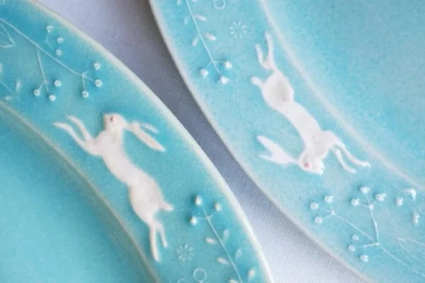 兩個Yoshizawa 益子燒綠色兔子花卉橢圓餐盤的特寫，展示邊緣的兔子和植物圖案 - Close-up of two Yoshizawa Mashiko-style green rabbit floral oval plates, showing the rabbit and plant patterns on the edges