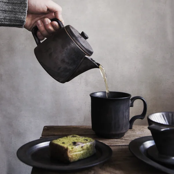 手握銅色 Ancient Pottery 陶瓷壺 - 倒茶入茶杯，桌上有蛋糕. Copper Teapot Pouring Tea into a Teacup with Cake.