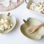 兩個開心果色Yoshizawa 益子燒蘋果小盤放在枱上的場景圖,一個裝配菜、一個放着叉子