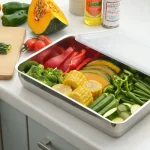 吉川不鏽鋼瀝水籃 L (大)尺碼，打開膠蓋子擱放在盒邊，裡面裝着不同蔬菜以作備菜之用