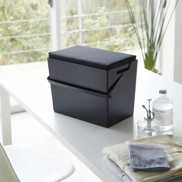 黑色款的 TOWER 熨斗收納箱放在房間的白色枱面上，背景可見窗外景色