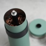 打開蓋子放在旁邊的日本製 CAPTAIN STAG 陶瓷刀手搖咖啡研磨器俯視圖，可看見罐內裝了咖啡豆