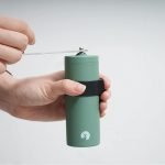 手上拿着日本製 CAPTAIN STAG 陶瓷刀手搖咖啡研磨器，示範示範攪磨咖啡豆的白色背景圖