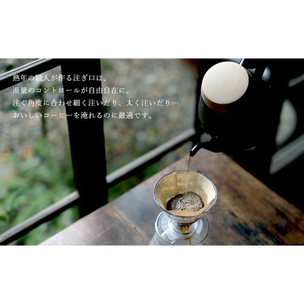 拿着黑色日本製 Ovject 搪瓷咖啡壺將水倒進木枱上的咖啡濾杯裏，背景是窗外景色。