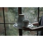 雙手捧着裝着白色日本製 Ovject 搪瓷咖啡壺與杯的圓形托盤，背景是窗外景色