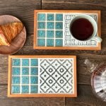 兩款不同設計的日本製 SATOMIMI 咖啡托盤放在木枱上，其中一款上面放着一杯咖啡，旁邊有一個裝着麵包的碟與一個咖啡壺