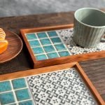 日本製SATOMIMI 咖啡托盤「銀杏」與「堇」款設計的托盤放在木枱上，銀杏款的托盤上放在一杯咖啡