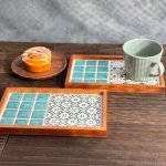 日本製SATOMIMI 咖啡托盤其中的 「堇 款 與銀杏款一起放在木枱上，銀杏款上放着一隻陶瓷杯子，枱上另有一碟甜品