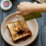 右手拿着綠色的蜜糖壺將蜜糖倒到碟子上的吐司上