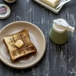 日本製Zero Japan 陶瓷蜂蜜壺綠色款放在木枱上的俯視圖，旁邊的疊紙上放着麵包