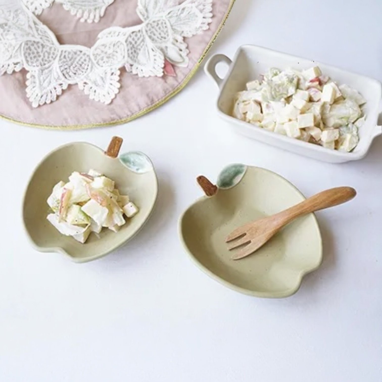 兩個紅色Yoshizawa 益子燒蘋果小盤放在枱上，旁邊放咗一本圖畫書，書上有蘋果及啤梨的圖案