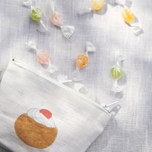 Isabelle Boinot 甜品 舟形亞麻小物包 平放在白色的布上，布上撒滿了很多糖。