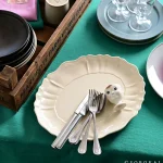 白色款 STUDIO M' Sobokai Communus 饗宴浮雕盤放在綠色枱上，盤裡面放了刀叉。