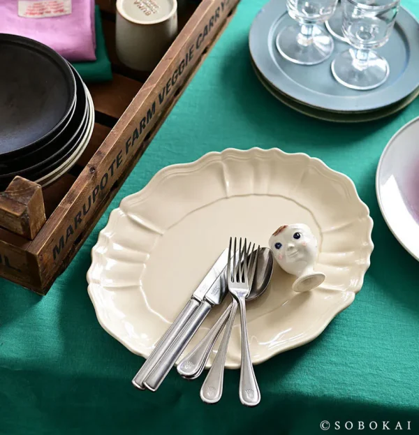白色款 STUDIO M' Sobokai Communus 饗宴浮雕盤放在綠色枱上，盤裡面放了刀叉。