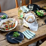 白色款 STUDIO M' Sobokai Communus 饗宴浮雕盤 (32.5cm) 裝着魚放在木餐桌上，桌上還有其他食物。