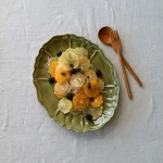 橄欖綠色款 STUDIO M' Sobokai Communus 饗宴浮雕盤 (32.5cm) 裝着食物放在木餐桌上的俯視圖，旁邊有木匙羹與叉子。