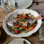 白色款 STUDIO M' Sobokai Communus 饗宴浮雕盤 (32.5cm) 裝着魚放在木餐桌上的俯視圖。