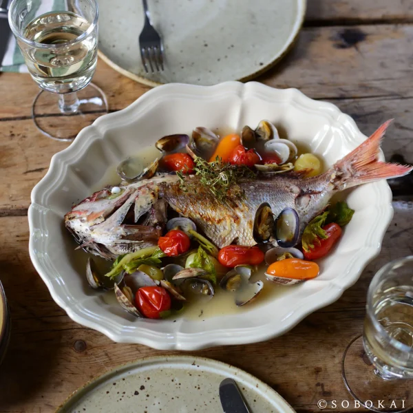 白色款 STUDIO M' Sobokai Communus 饗宴浮雕盤 (32.5cm) 裝着魚放在木餐桌上的俯視圖。