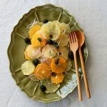 橄欖綠色款 STUDIO M' Sobokai Communus 饗宴浮雕盤 (32.5cm) 裝着水果沙律放在木餐桌上的俯視圖，盤上有木匙羹與叉子。