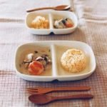 二個 Studio M' Aeroport 雙格盤裝着食物放在枱上，旁邊放了一把叉與匙羹。