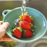 把裝在薄荷綠款 Studio M’ Berry 雙耳瀝水碗裡面的草莓直接放在水龍頭下沖洗。