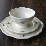 深色木餐枱上有一個 Studio M' Early Bird 小碗放在二個不同尺寸的圓碟上。