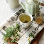 Studio M' Early Bird 燕子系列茶杯裡裝着茶，放了一把小匙羹放在枱面的報紙上的俯視圖。