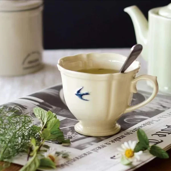 Studio M' Early Bird 燕子系列茶杯裡裝着茶，放了一把小匙羹放在枱面的報紙上。