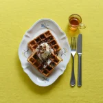 黃色枱上的一個 Studio M' Mignardises 餐盤裝着二塊窩夫,餐盤旁邊放了刀叉與一杯茶。