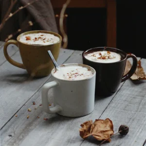 三種不同顏色的 Studio M' Mountain 直角手柄粗陶杯裝滿飲品放在木枱上