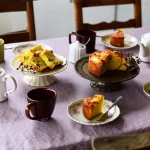 Studio M' Parler 花瓣高腳托盤 24cm 古銅色與白色款托盤裝着蛋糕與其他餐具一起放在餐桌上 。