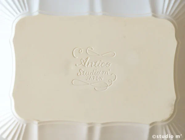 白色 tudio M' Antico 烤盤的底部特寫，可見刻着品牌 logo。